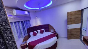 A modern bedroom with a circular bed, a ceiling fan, an air conditioning unit, and a wooden door. - HOTEL SAVERA (Ahmedabad)