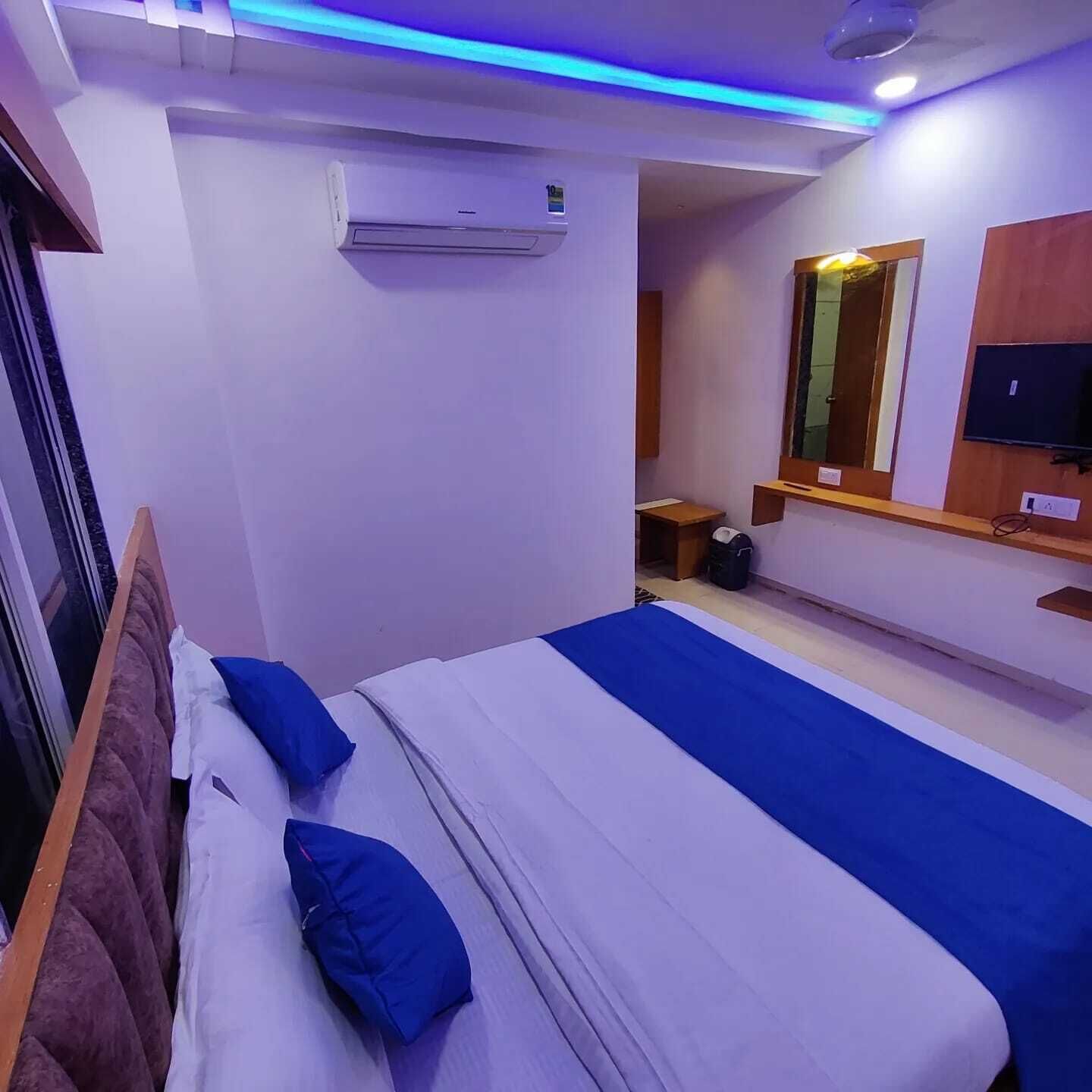 A hotel room with a bed, a small table, a mirror, and a TV.