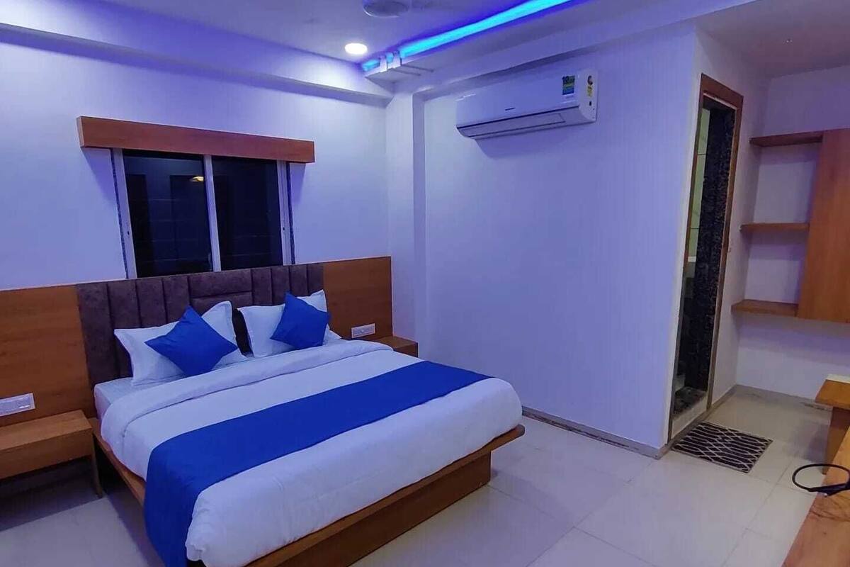 A bedroom with a bed, a nightstand, an air conditioning unit, a ceiling fan, and a window.