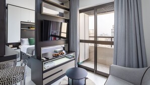 Una habitación de hotel moderna con balcón, un escritorio con computadora, una silla y una cama con televisor encima.