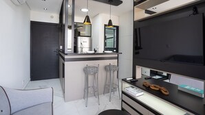 Una cocina moderna con encimera negra, dos taburetes de bar, un refrigerador y un microondas.