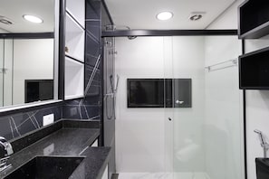 A modern bathroom with a glass-enclosed shower, a large mirror, and a black countertop. - Jardins by Conviva (São Paulo)