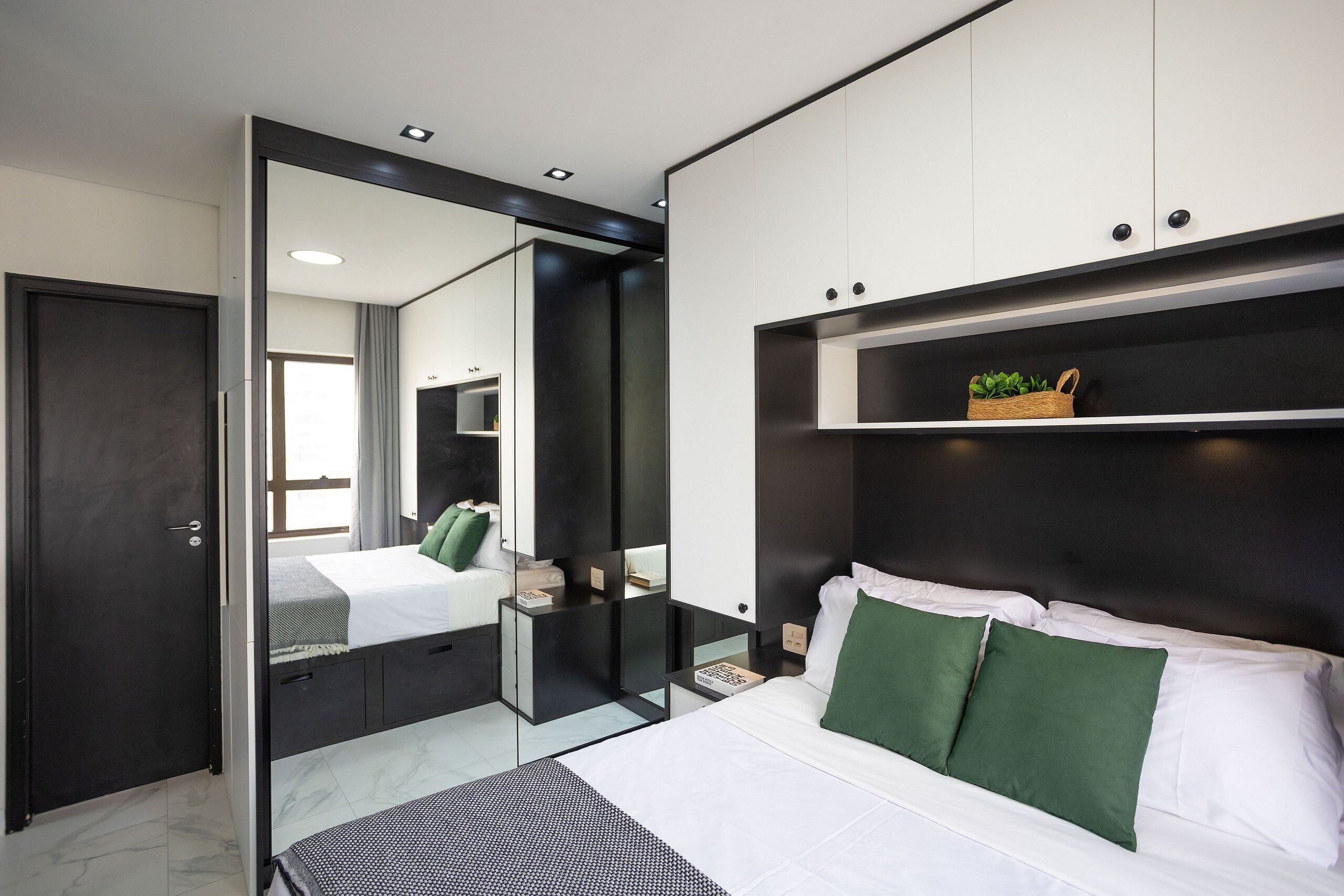 A modern bedroom with a large bed, a bedside table, a mirror, and a wardrobe.