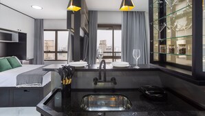 Una habitación de hotel moderna con una cama, una zona de cocina con un lavamanos y un comedor con una vitrina de copas de vino.
