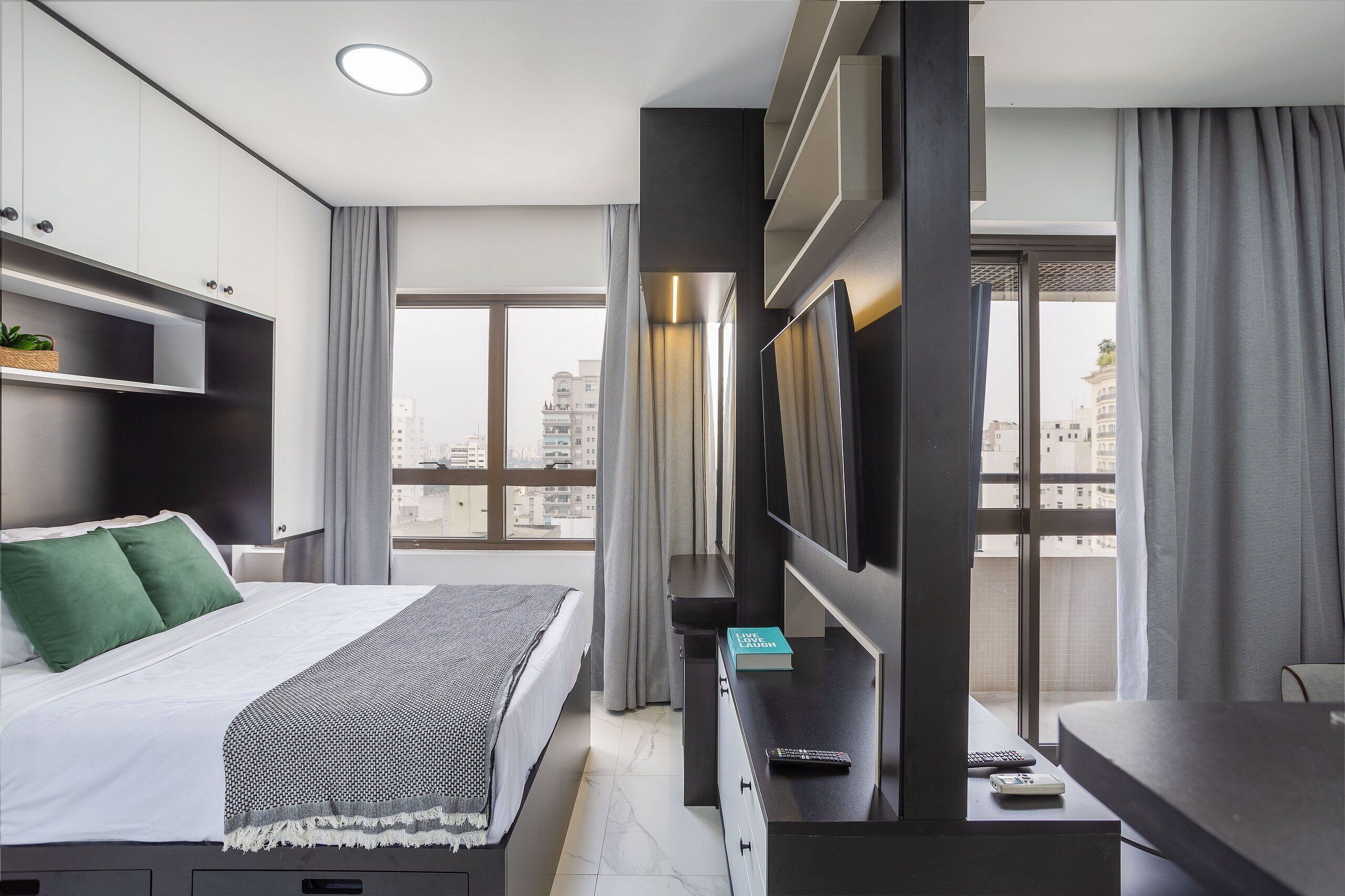 A modern hotel room with a bed, a TV, a desk, and a view of the city.