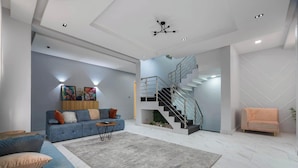 A modern living room with a blue sofa, a grey rug, a staircase, and a small orange armchair. - Bizzare Luxury Apartment (Abuja)
