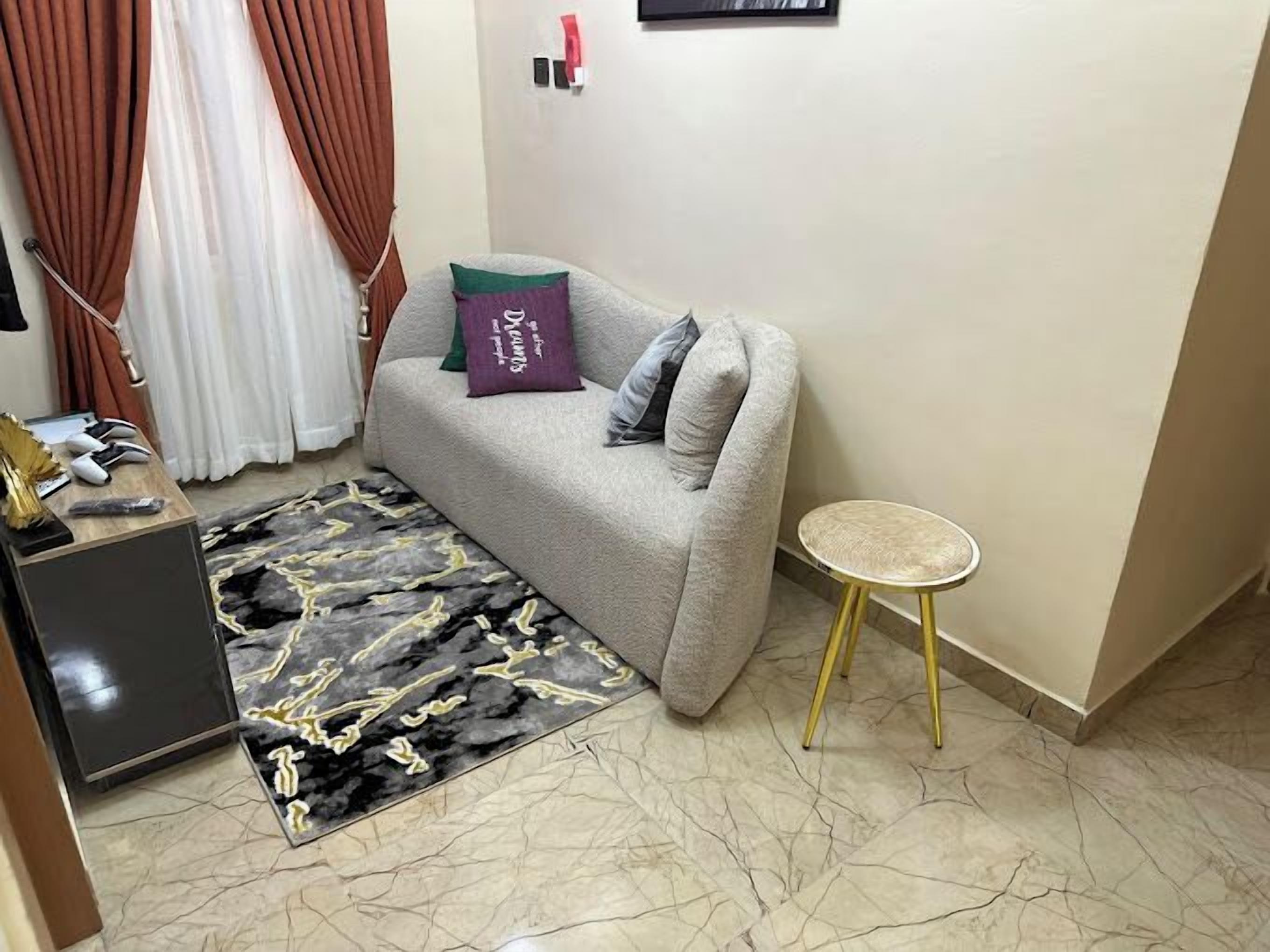 A living room with a grey sofa, a small round table, a patterned rug, and a TV stand.