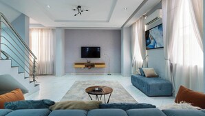 A modern living room with a sofa, a coffee table, a TV, and a staircase. - Bizzare Luxury Apartment (Abuja)