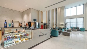 A modern hotel lobby with a coffee station, seating area, and large windows. - Rhenium Hotel (Riyadh)