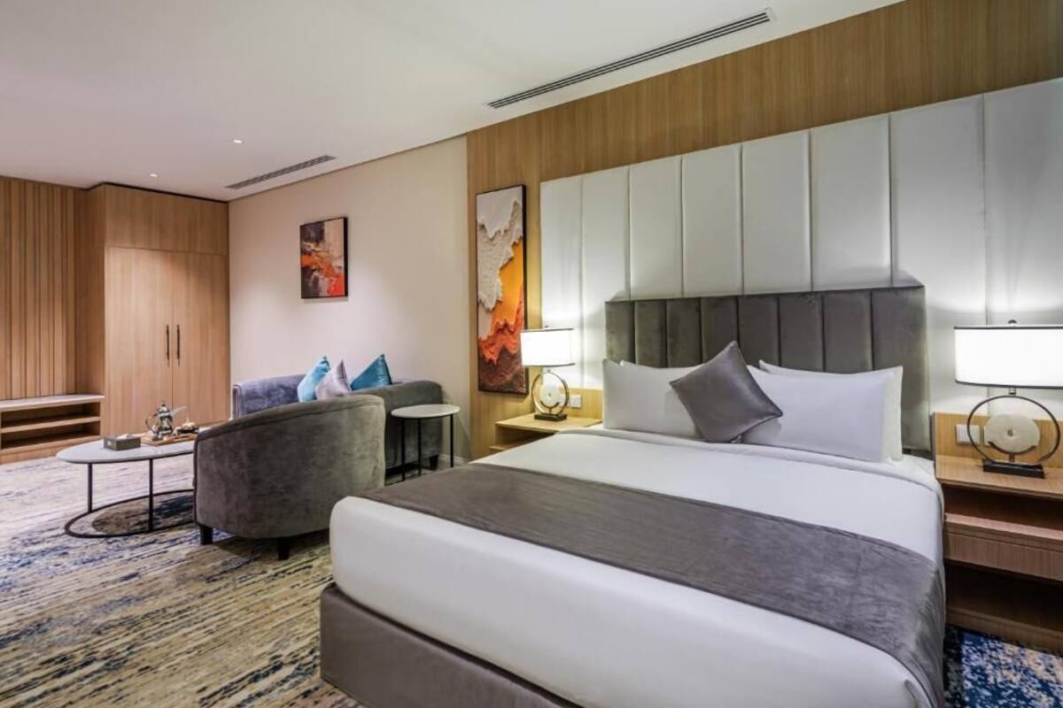 A hotel room with a large bed, a sofa, a small table, and a cabinet.
