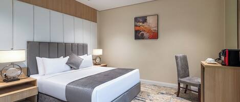 A hotel room with a large bed, bedside tables, a chair, a desk, and a painting on the wall.