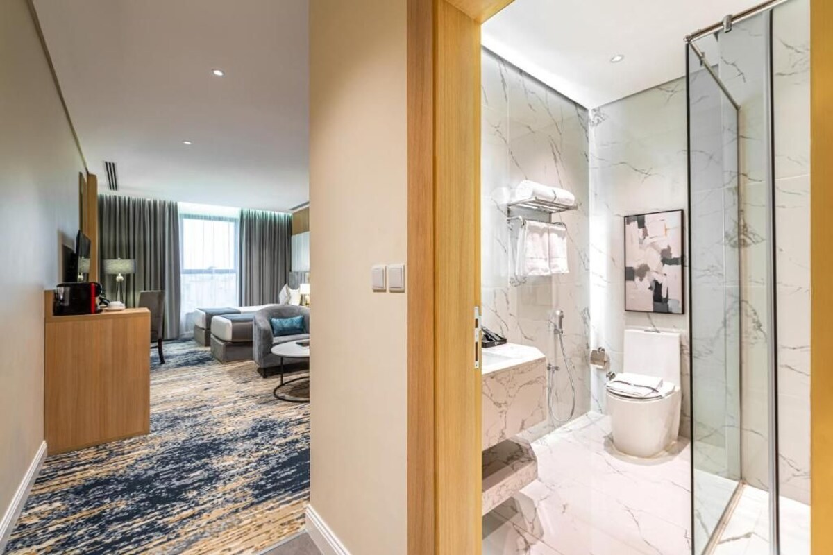 A hotel room with a marble bathroom, a sitting area with a sofa and coffee table, and a view of the city through large windows.