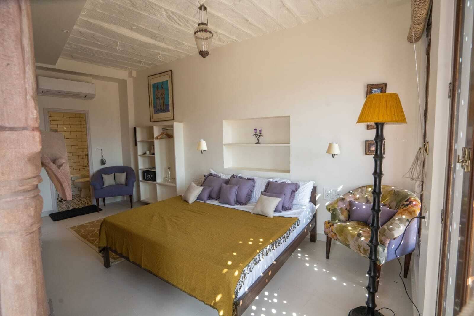 A bedroom with a bed, a chair, a lamp, and a shelf with decorative items.