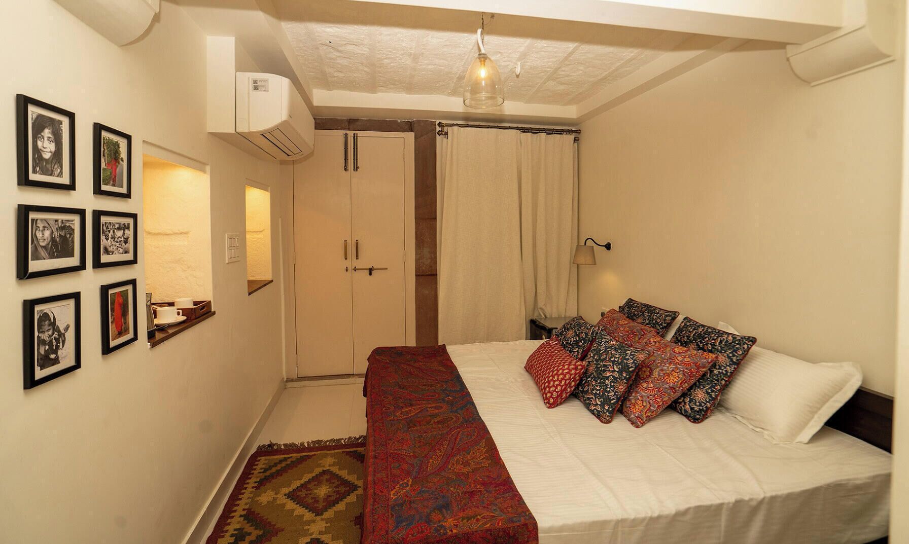 A bedroom with a bed, a wardrobe, a bedside table, and a wall-mounted air conditioner.
