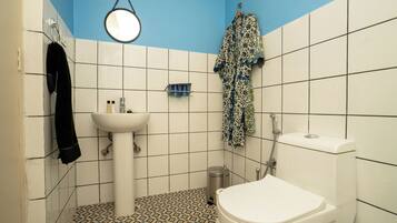 A bathroom with a white sink, toilet, and shower. There is a towel rack with a towel and a hanging robe. A mirror is mounted on the wall above the sink.