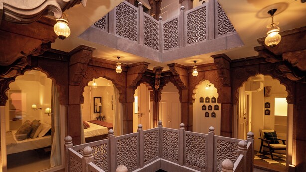 A traditional interior with ornate wooden arches, a central balcony with intricate railings, and a bed with a view. - Aakash Heritage Haveli (Jodhpur)