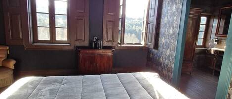 A bedroom with a large bed, two windows, a wooden ceiling, and a view of the outdoors.