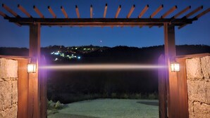 Un arco in pietra con una pergola in legno sopra, che conduce a una zona pavimentata.