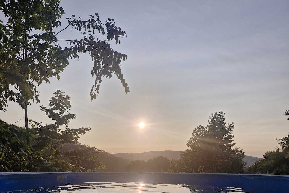 En lugn utomhuspool med fri utsikt över solnedgången bakom träden.