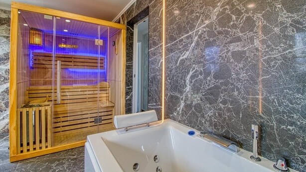 Moderni kylpyhuone, jossa on marmoriseinä, puinen sauna ja suuri kylpyamme.