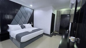 A modern hotel room with a large bed, a dark headboard, a flat-screen TV, and a minibar.