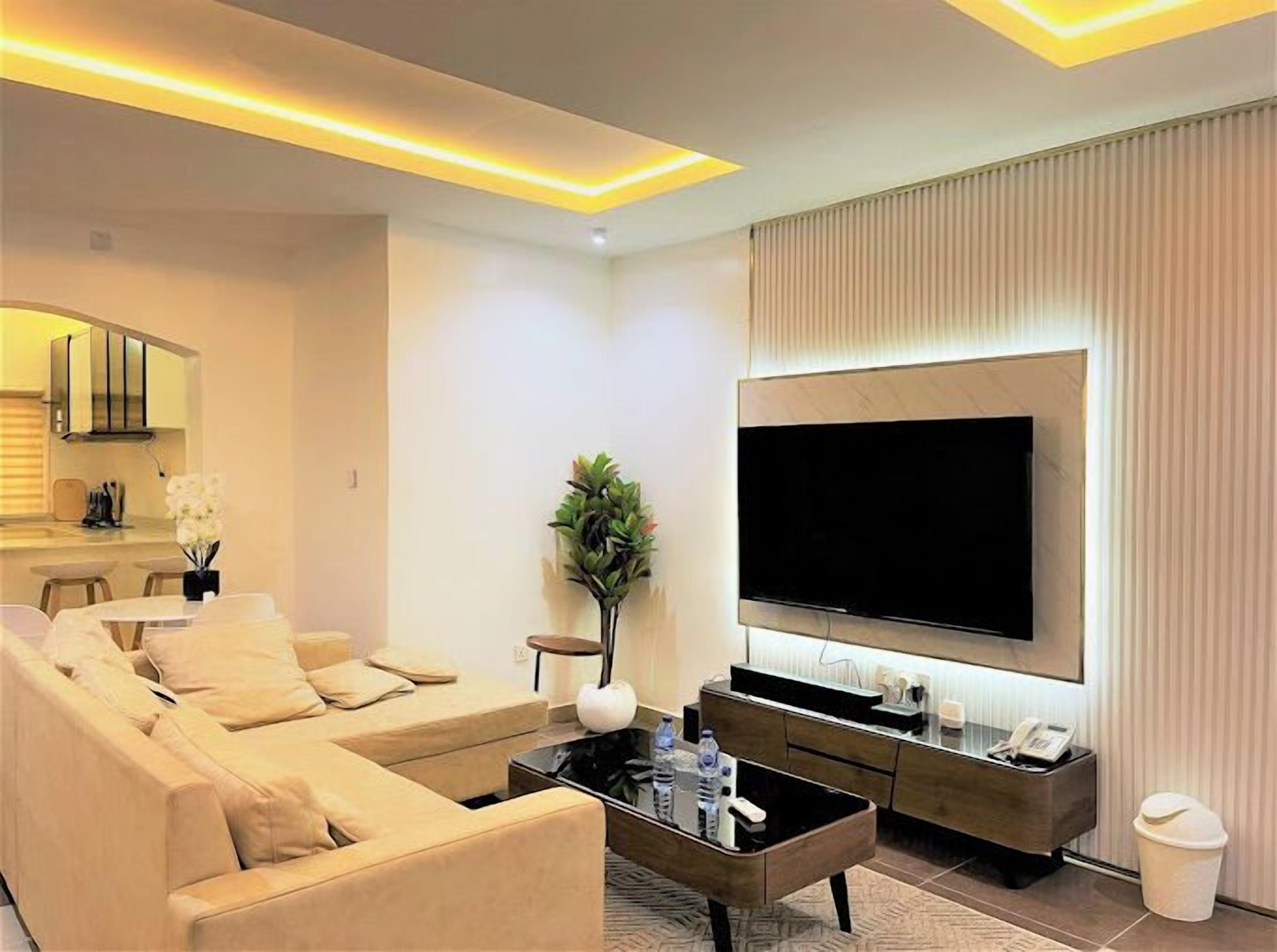 A modern living room with a large flat-screen TV, a sofa, a coffee table, and a small side table with a plant.