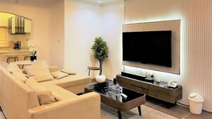 A modern living room with a large flat-screen TV, a sofa, a coffee table, and a small side table with a plant.