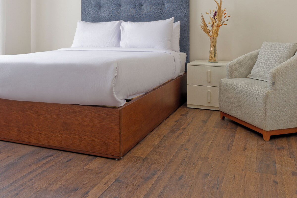 A bedroom with a bed, bedside table, chair, and a hanging light fixture.