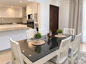 Cozinha moderna com armários brancos, bancada preta e um espaço de refeições com mesa preta e cadeiras brancas.
