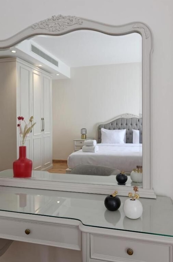 A bedroom with a large mirror, a bed with white bedding, a nightstand, and a dresser with a vase.