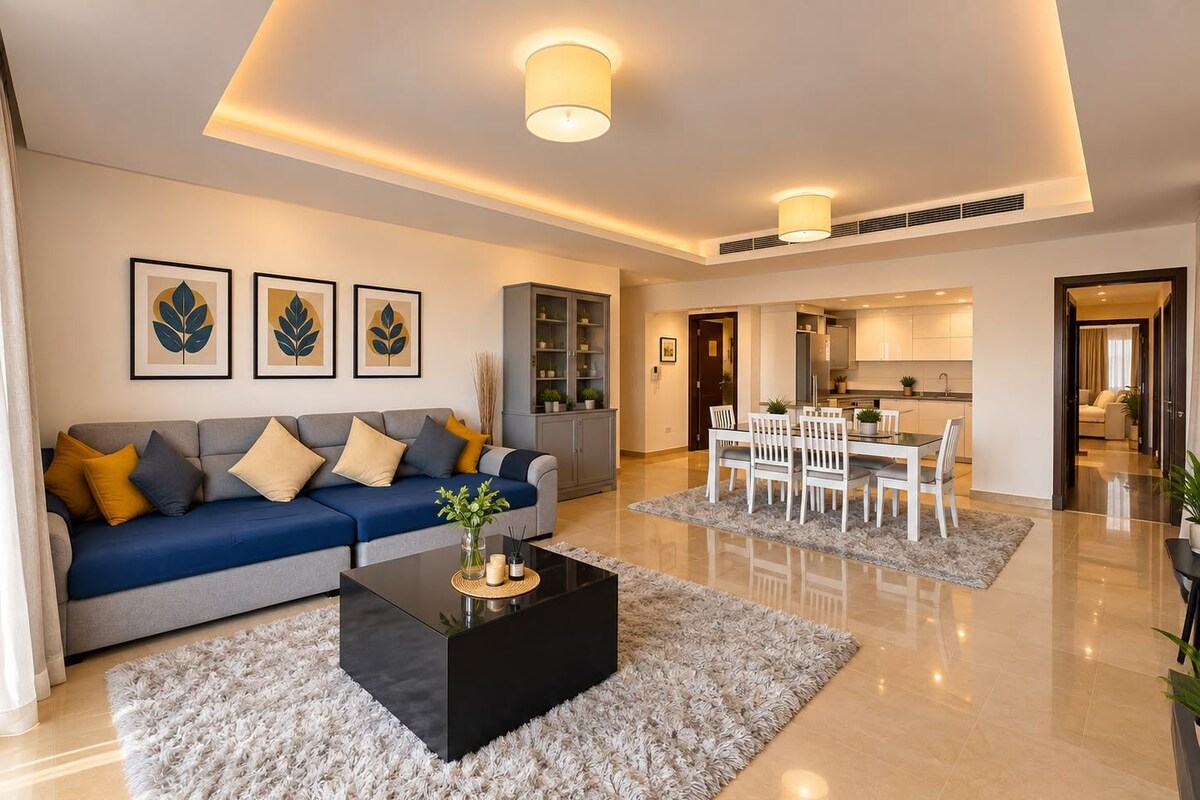 Een moderne woonkamer met een bank, salontafel en een eethoek. Er hangen ingelijste foto's aan de muur, een kast en een keuken is zichtbaar op de achtergrond.