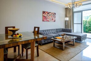 A modern living room with a glass dining table, grey sofa, and a painting on the wall.