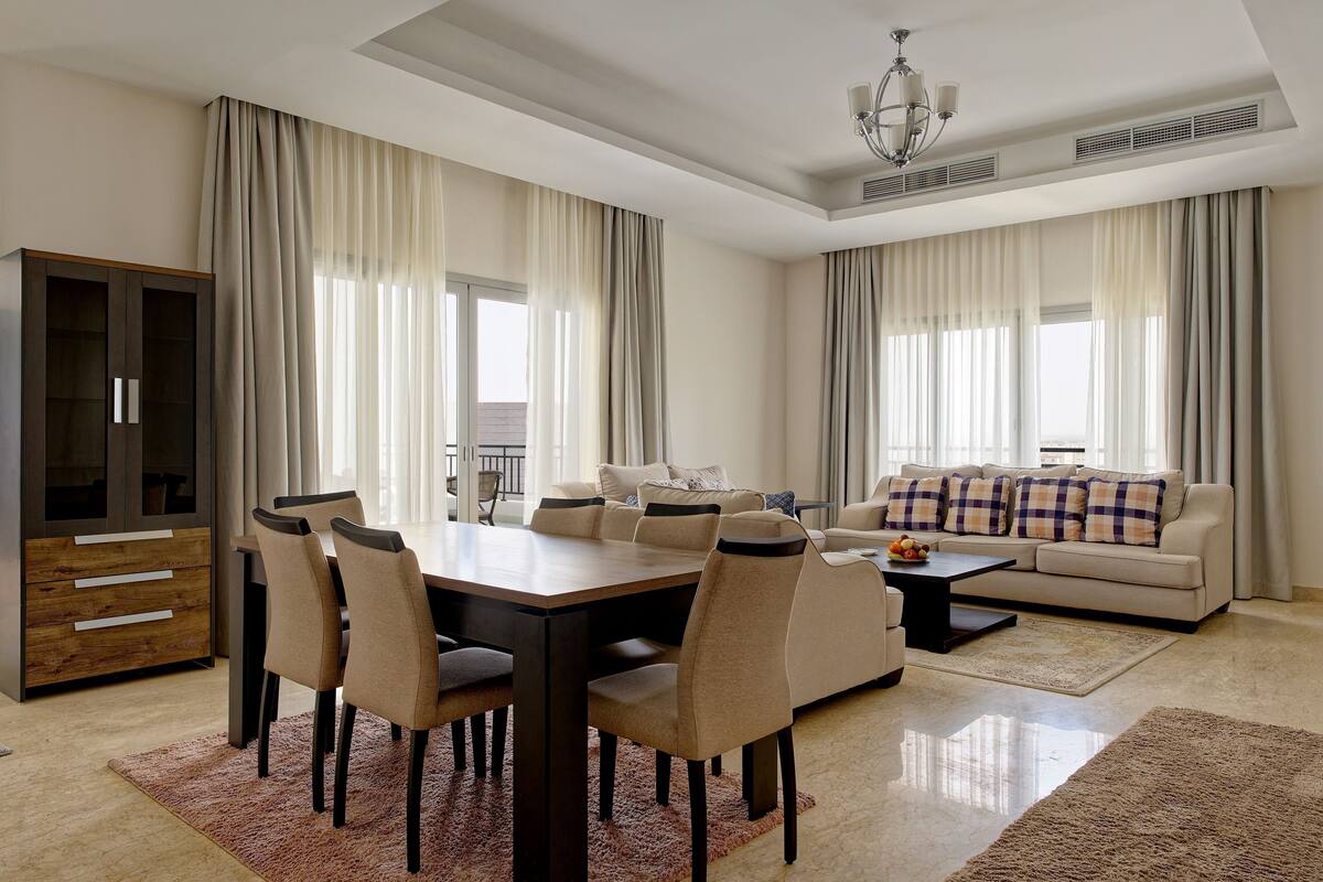 A modern living room with a dining area, large windows, and a sofa with decorative pillows.