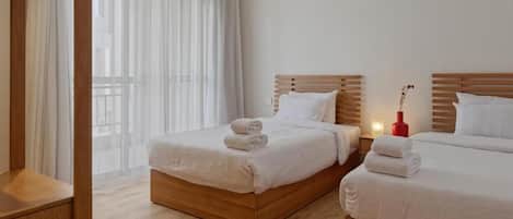 A hotel room with two beds, wooden headboards, white bedding, and a view through sheer curtains.