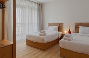 Ein Hotelzimmer mit zwei Betten, Holzkopfteilen, weißer Bettwäsche und Blick durch transparente Vorhänge.