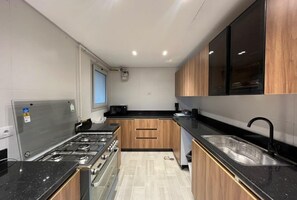 A modern kitchen with a gas stove, oven, and black countertops. - VESTA - Cairo Festival City Residence (New Cairo)