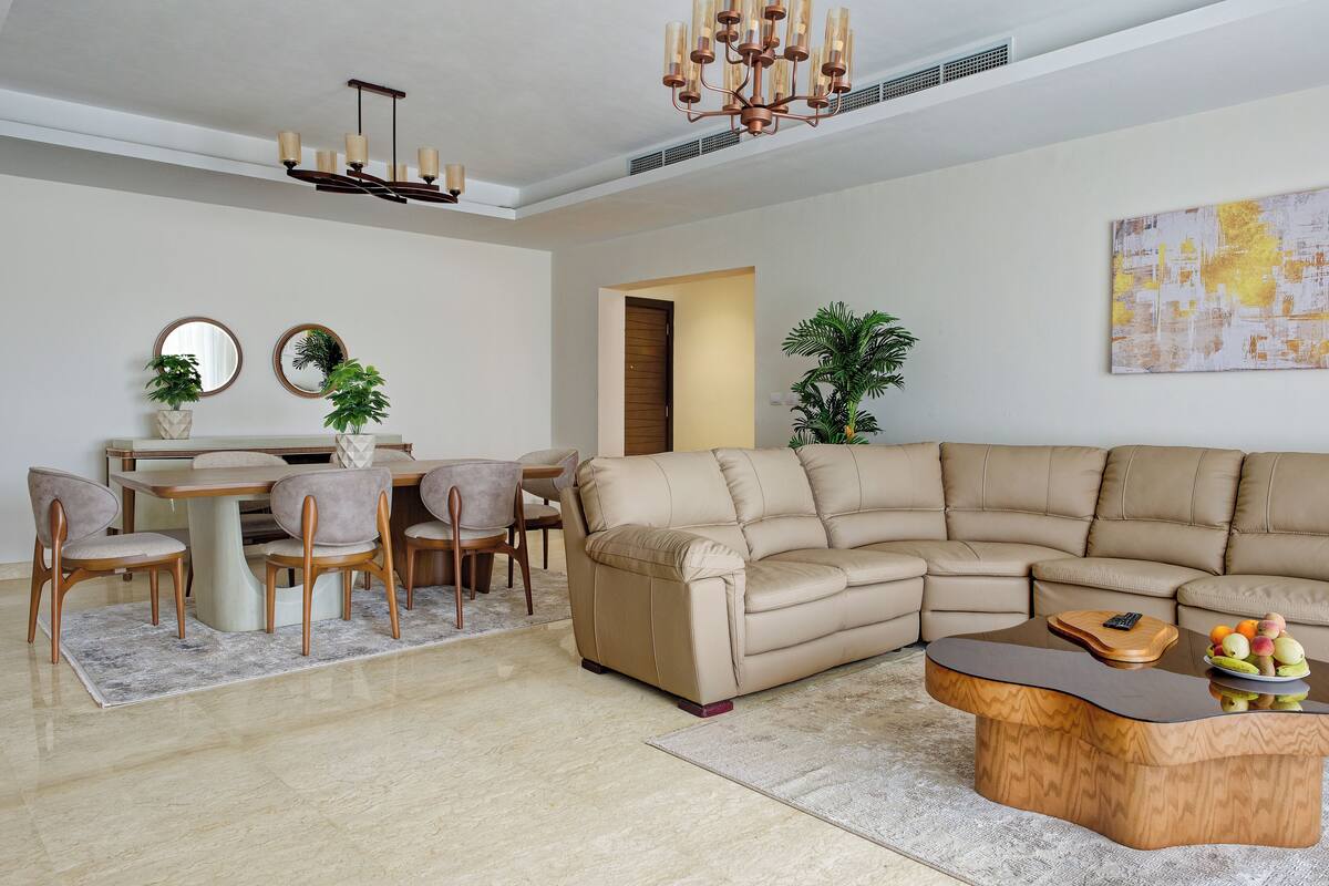 A modern living room with a sectional sofa, a dining table with chairs, and a coffee table with fruit.