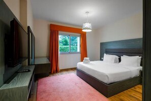 Habitación de hotel con cama, televisor, ventana con cortinas e iluminación en el techo.
