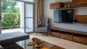 A modern living room with a grey sofa, a glass coffee table, a wooden entertainment unit, and a flat-screen TV. - VESTA - Cairo Festival City Residence (New Cairo)