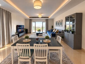 A modern living room with a dining area, a television, and a balcony with a view.