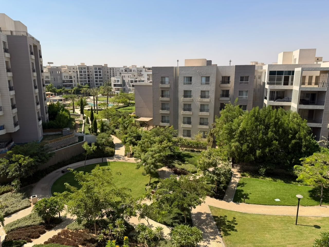 A residential complex with multiple apartment buildings, landscaped gardens, and a clear sky.