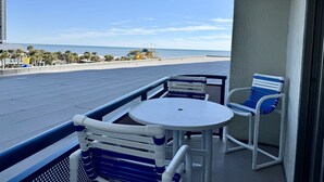 Un balcon avec deux chaises et une table, donnant sur une plage et un parking.