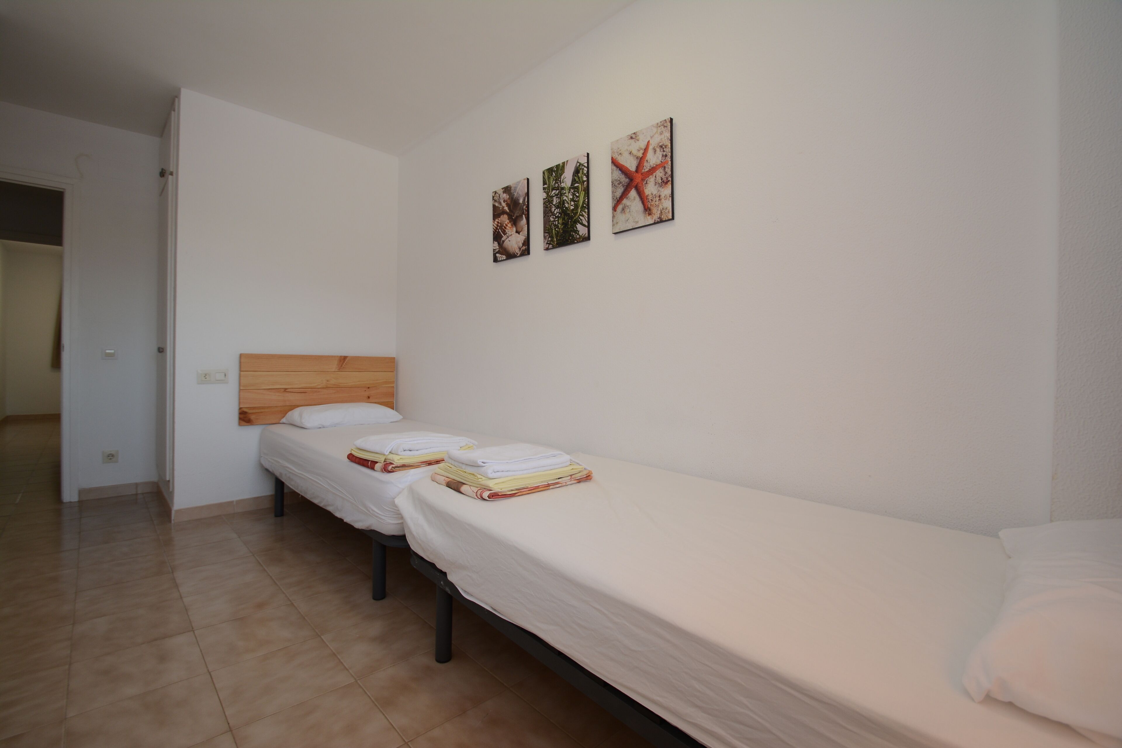 A room with two single beds, a wooden headboard, and three wall-mounted pictures.