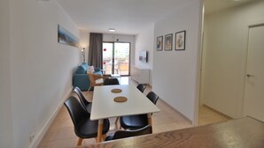 Un salon moderne avec une table à manger blanche, des chaises noires, un canapé bleu et un coin cuisine à l’arrière-plan.