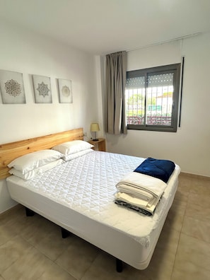 A neatly made bed with a quilted cover, a wooden headboard, and a nightstand with a lamp. There are three wall art pieces above the bed. - Sa Gavina Estartit (Torroella de Montgrí)
