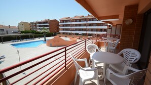 Un balcon avec des chaises et une table en plastique blanc, donnant sur une piscine et un immeuble doté de nombreux balcons.