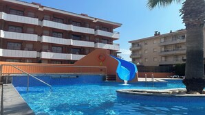 Une piscine avec un toboggan bleu, entourée d’immeubles à plusieurs étages dotés de balcons.