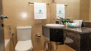 A bathroom with a toilet, sink, and shower. There are towels hanging on the wall and a trash can.
