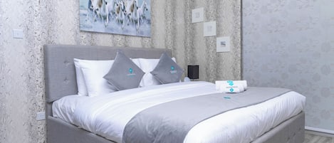 Um quarto moderno com uma cama grande, roupa de cama cinza e uma pintura de cavalos na parede.