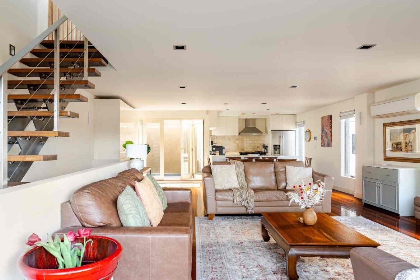 Een moderne woonkamer met een trap, een zithoek, een salontafel, en een keuken op de achtergrond.